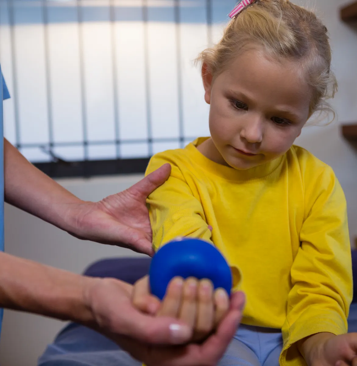 Pediatric physical therapy: Child holds ball during rehab treatment. Improve function, mobility recovery. Pain relief at our clinic.