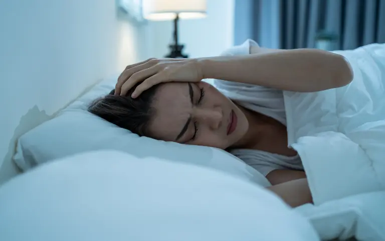 Head pain treatment: Woman in bed seeking pain relief. Physical therapy for neck pain relief and mobility recovery.