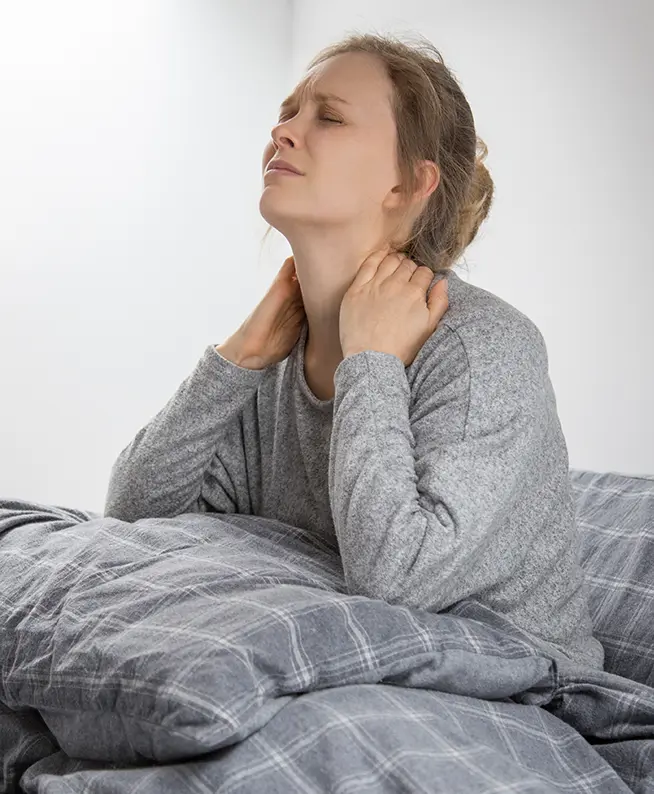 Neck pain relief: Woman on bed seeking work injury rehab. Physical therapy for mobility recovery at our rehabilitation clinic.