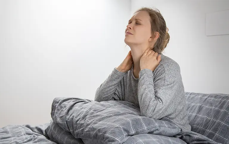 Neck pain relief: Woman on bed seeking work injury rehab. Physical therapy for mobility recovery at our rehabilitation clinic.