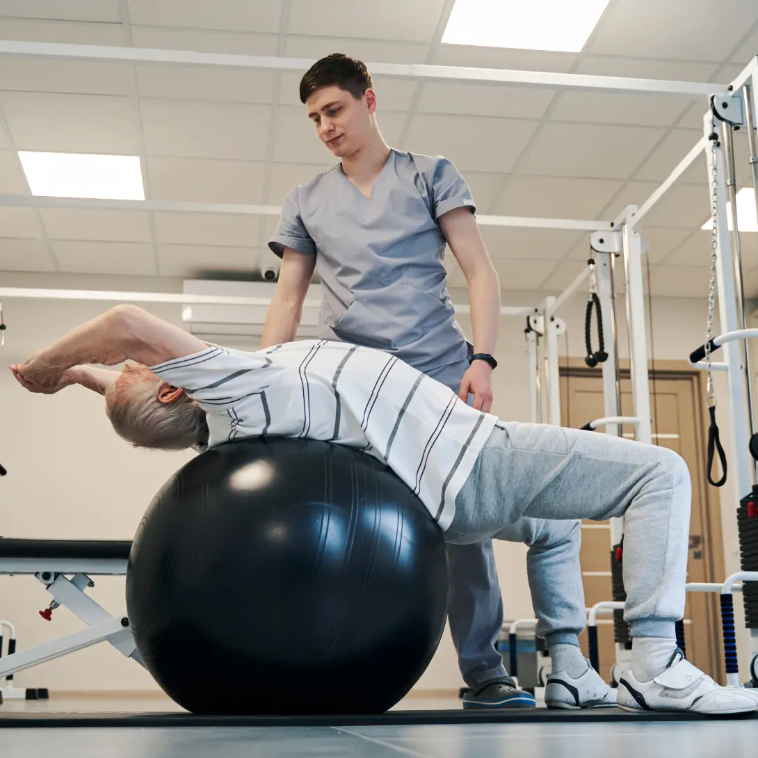 Work injury rehab: Patient improving mobility with balance ball exercise. Physical therapy for pain relief and faster recovery.
